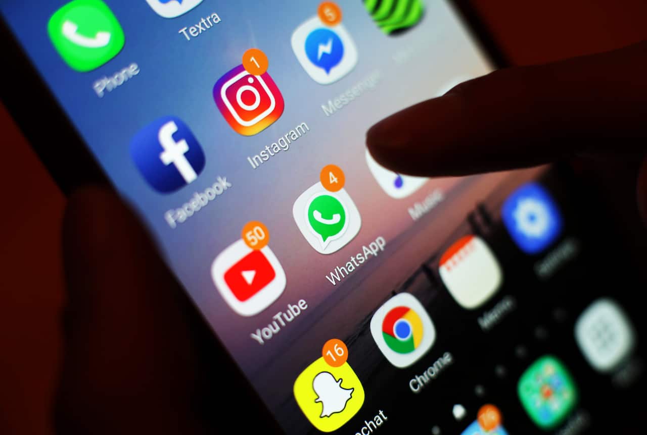 Una silueta del dedo de una persona está descansando en la pantalla del teléfono, mostrando aplicaciones y notificaciones en las redes sociales.