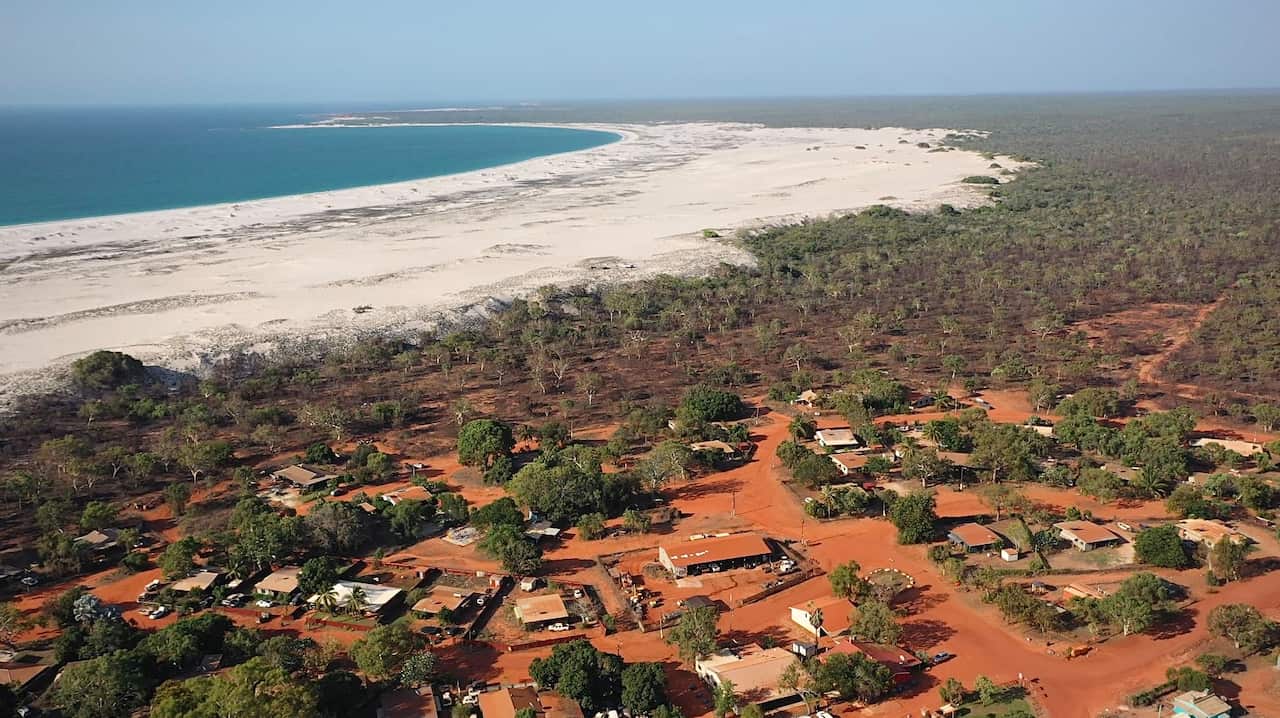 Drone vision showing blue ocean, white sand, and the red dirt of a remote Indigenous community.